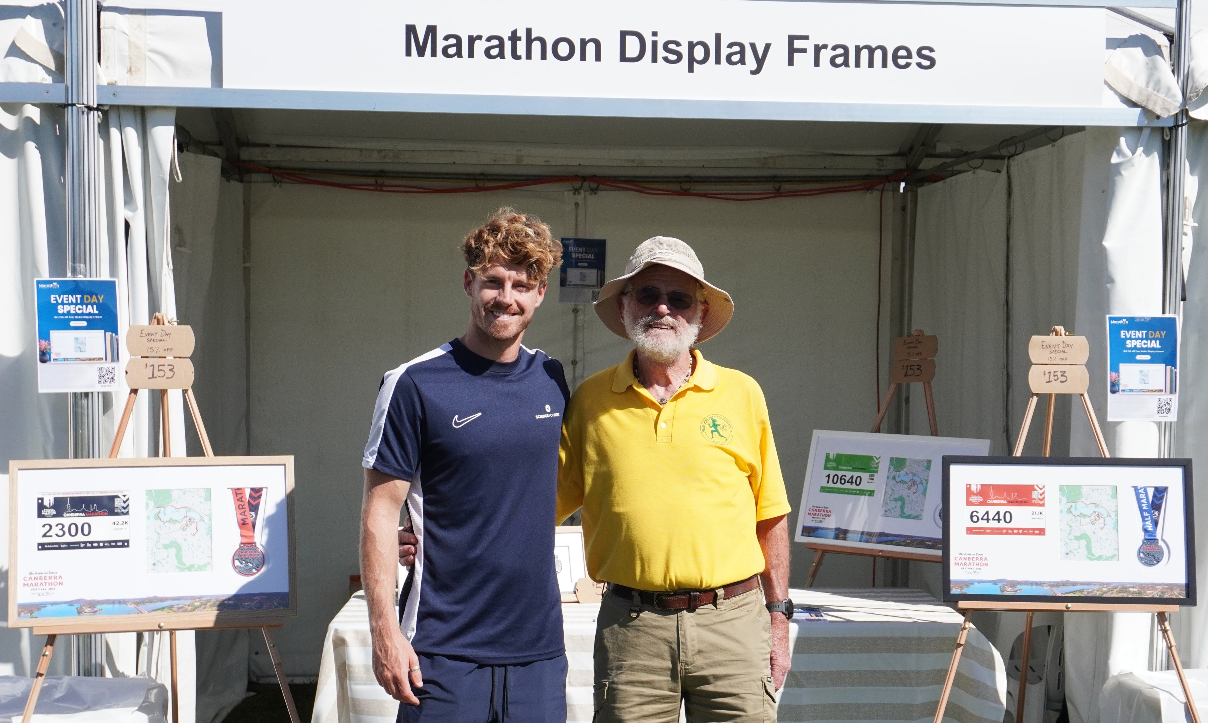 Two men standing in front of marathon display frames at an event.